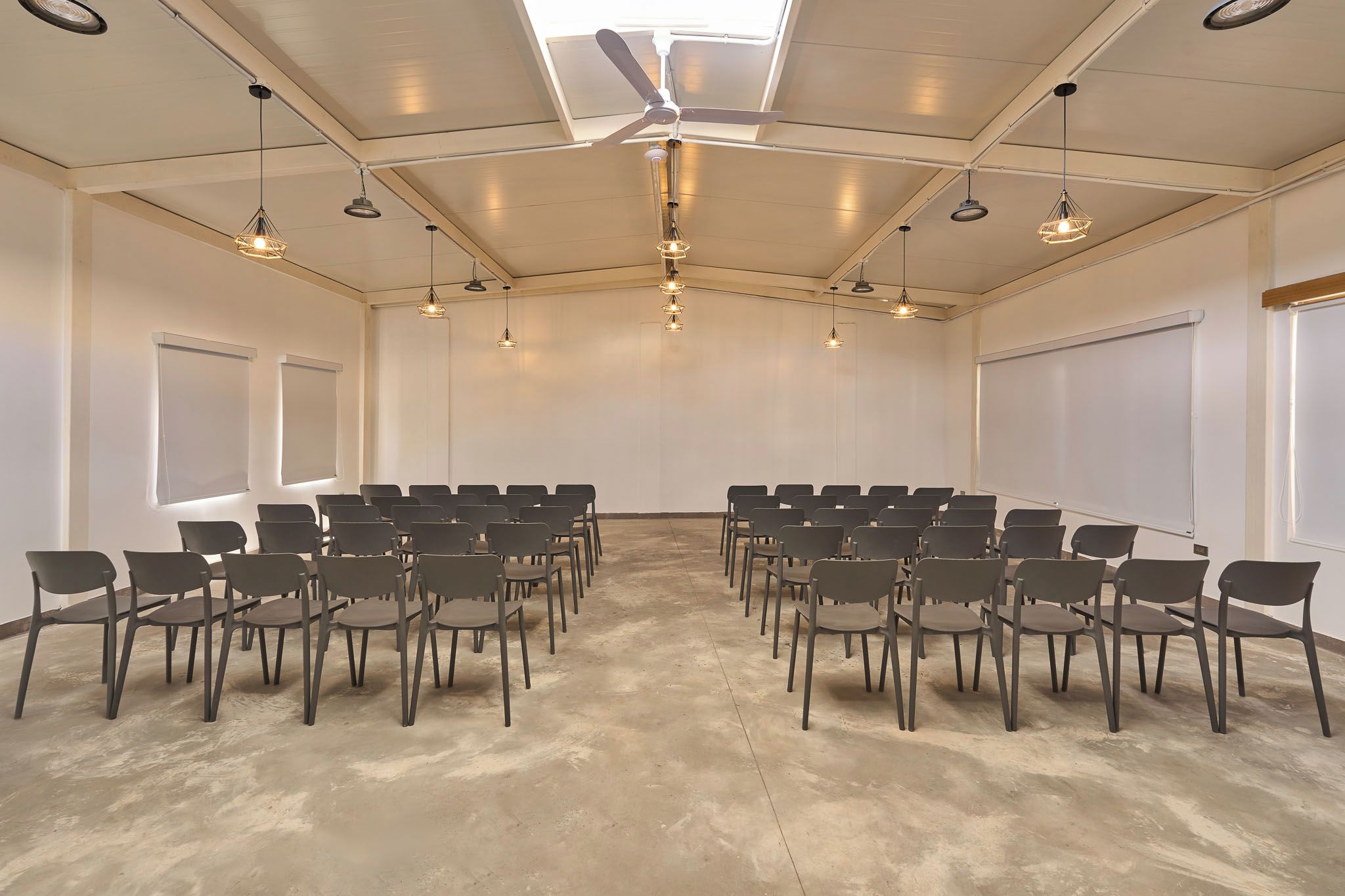A conference room with rows of chairs, a ceiling fan, and pendant lights.