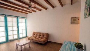 Una habitación con un sofá marrón, una mesita blanca pequeña y un ventilador de techo.