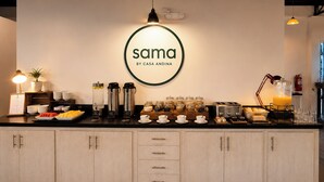 Una barra de desayuno con un letrero que dice 'sama by casa anadina', máquinas de café, un tostador y diversos productos para el desayuno.