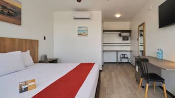 A hotel room with a bed, a desk, a chair, a TV, and an air conditioning unit.