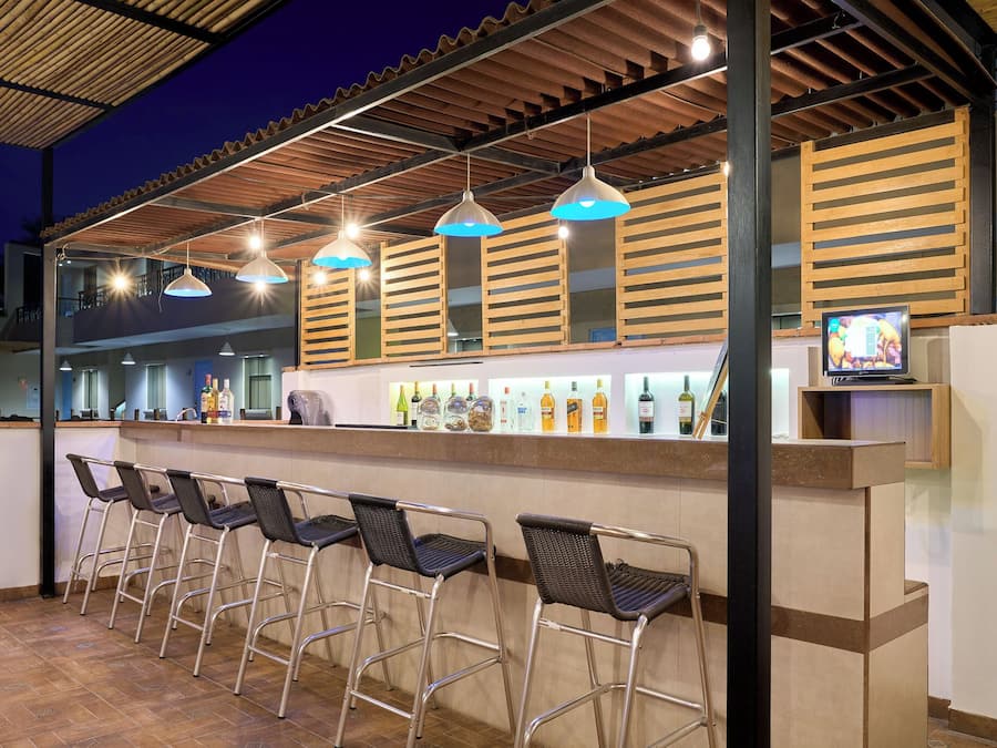 An outdoor bar area with metal chairs, a counter with bottles, and hanging pendant lights.