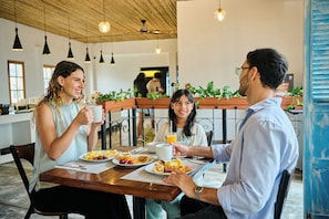 A group of people dining at a wooden table in a cafe with hanging lights and potted plants. - Casa Andina Standard Ica   (Ica)