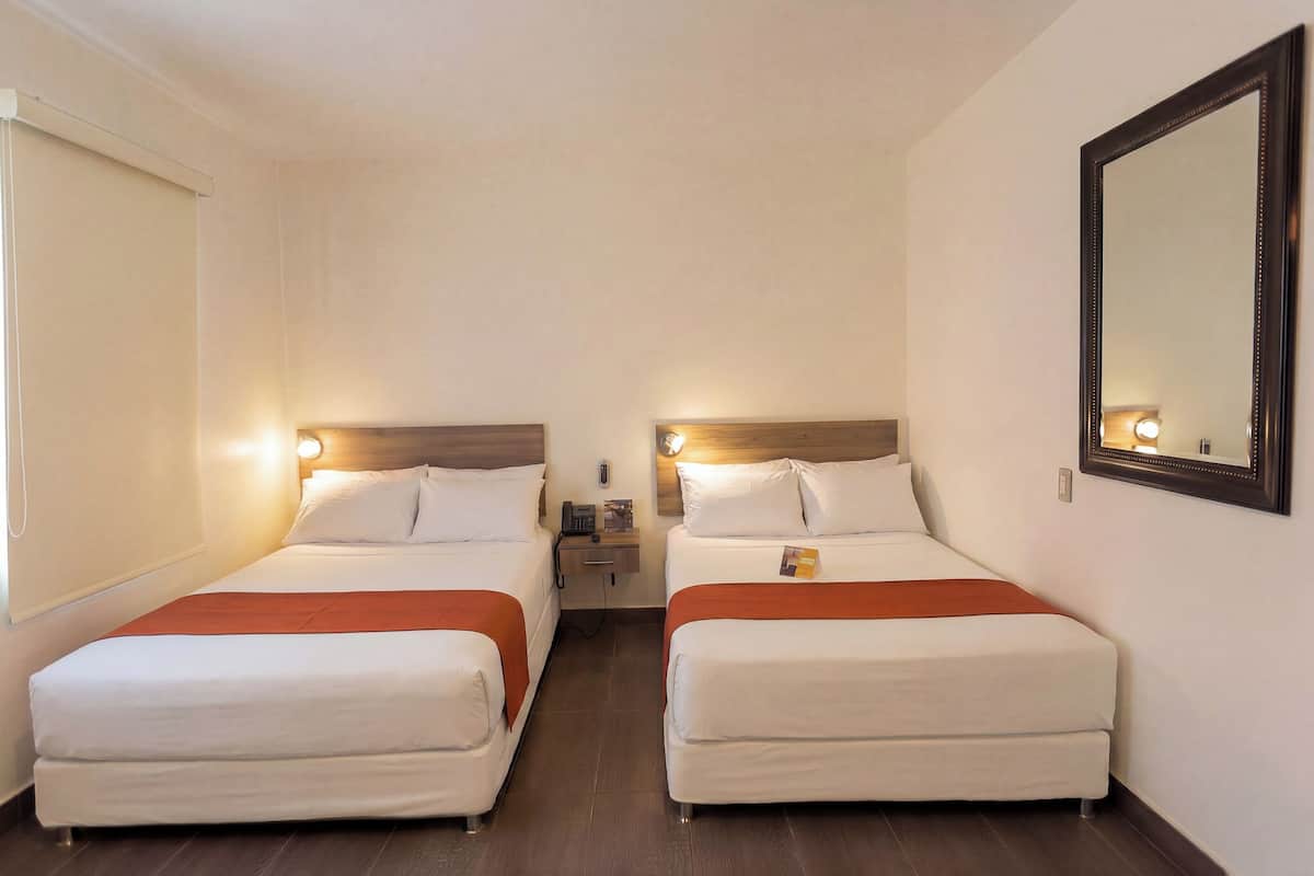 A hotel room with two beds, a nightstand, a mirror, and a window with blinds.