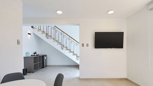 Un interior moderno con una escalera, un comedor y un televisor de pantalla plana montado en la pared.