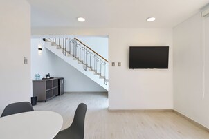 Un interior moderno con una escalera, un comedor y un televisor de pantalla plana montado en la pared.