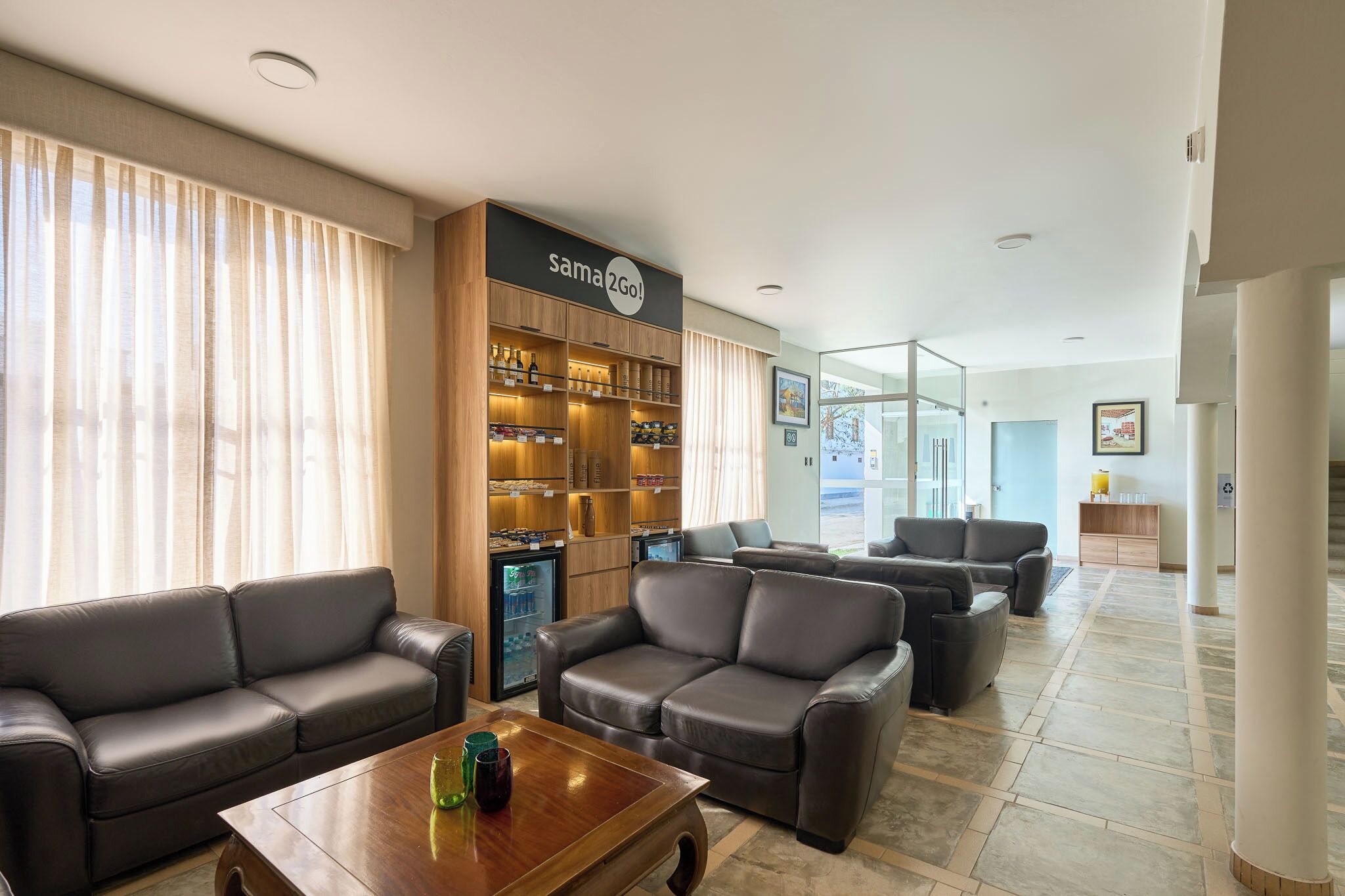 A hotel lobby with leather sofas, a coffee table, a minibar, and a Sam's Club sign.
