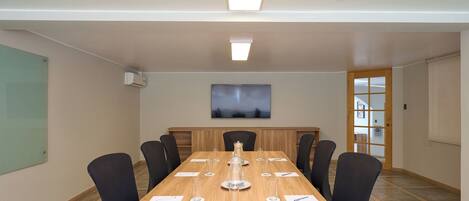 Un salón de conferencias con una mesa larga, sillas, una pantalla de proyector y una puerta con ventanal.