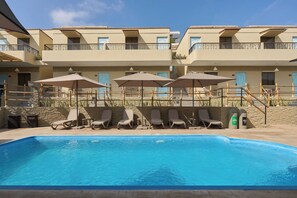 A swimming pool with lounge chairs and umbrellas, surrounded by a building with balconies and a stone wall. - Casa Andina Standard Ica   (Ica)