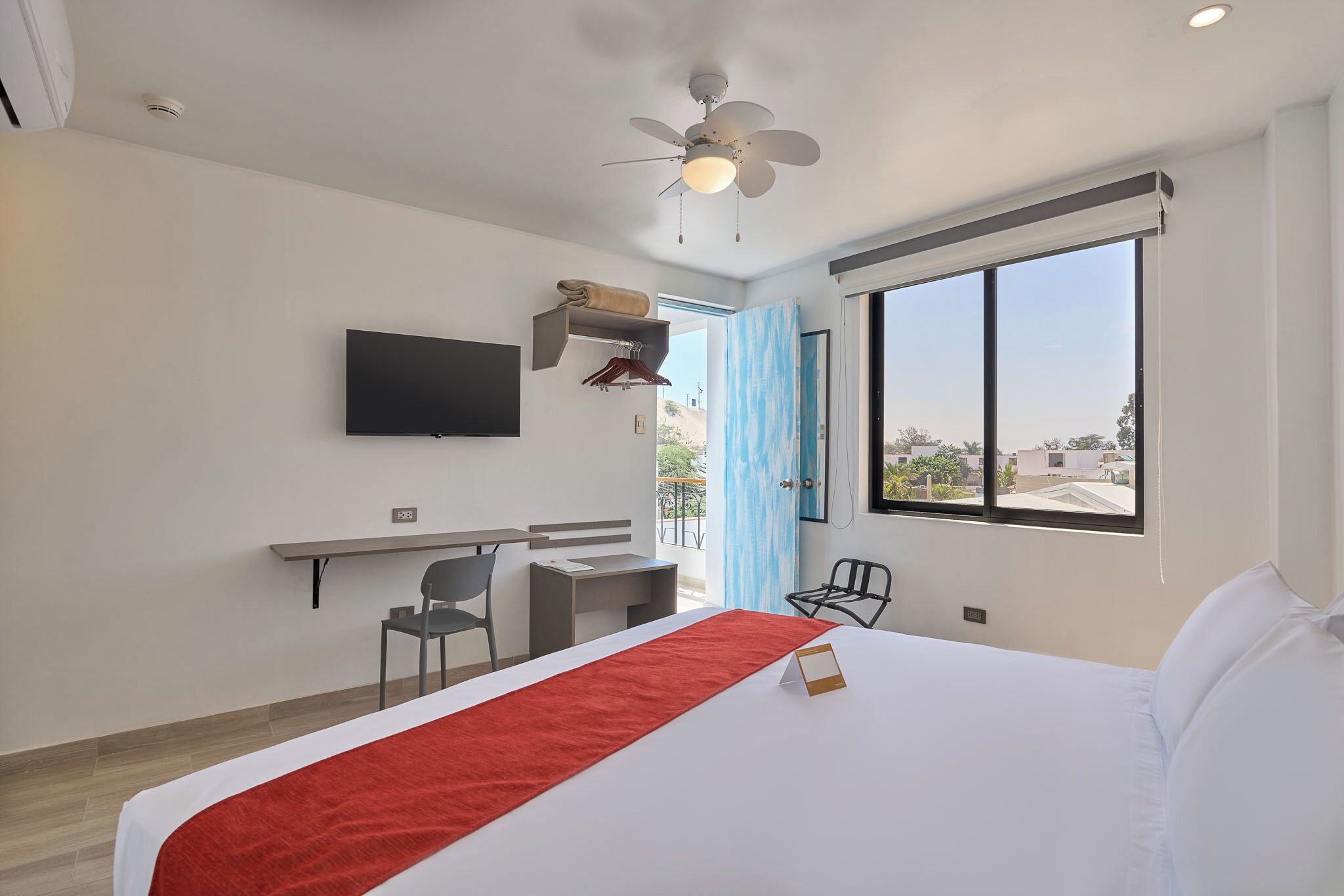 A hotel room with a bed, a desk, a chair, a television, and a large window.