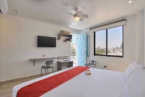 Habitación de hotel con cama, escritorio, silla, televisor y un amplio ventanal.