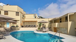 A swimming pool with sun loungers and umbrellas, surrounded by buildings with balconies. - Casa Andina Standard Ica   (Ica)