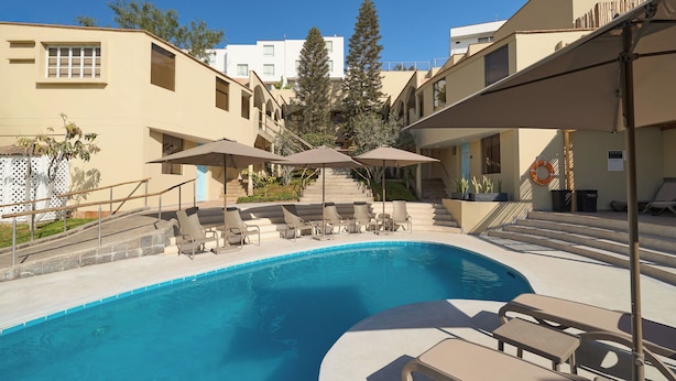 A swimming pool with lounge chairs and umbrellas, surrounded by buildings with a modern design. - Casa Andina Standard Ica   (Ica)