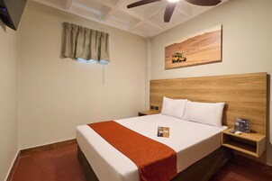 Habitación de hotel con una cama grande, un cabecero de madera, una mesita de noche y un ventanal con cortinas, además de una decoración de temática desértica.