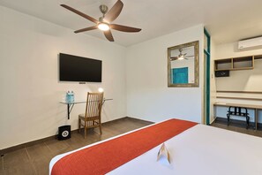 A hotel room with a bed, a ceiling fan, a mounted TV, a chair, a small table with water bottles, and a mirror. - Casa Andina Standard Ica   (Ica)