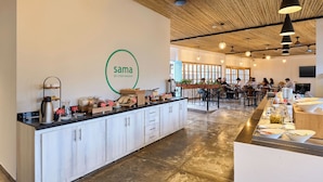 A modern cafe interior with a wooden ceiling, a central island with food items, and a logo on the wall. - Casa Andina Standard Ica   (Ica)