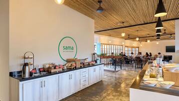 L’intérieur d’un café moderne, avec un plafond en bois, un îlot central où sont présentés les plats, et un logo sur le mur.