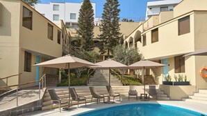 A swimming pool with lounge chairs and umbrellas, surrounded by buildings with steps leading up to a terrace. - Casa Andina Standard Ica   (Ica)