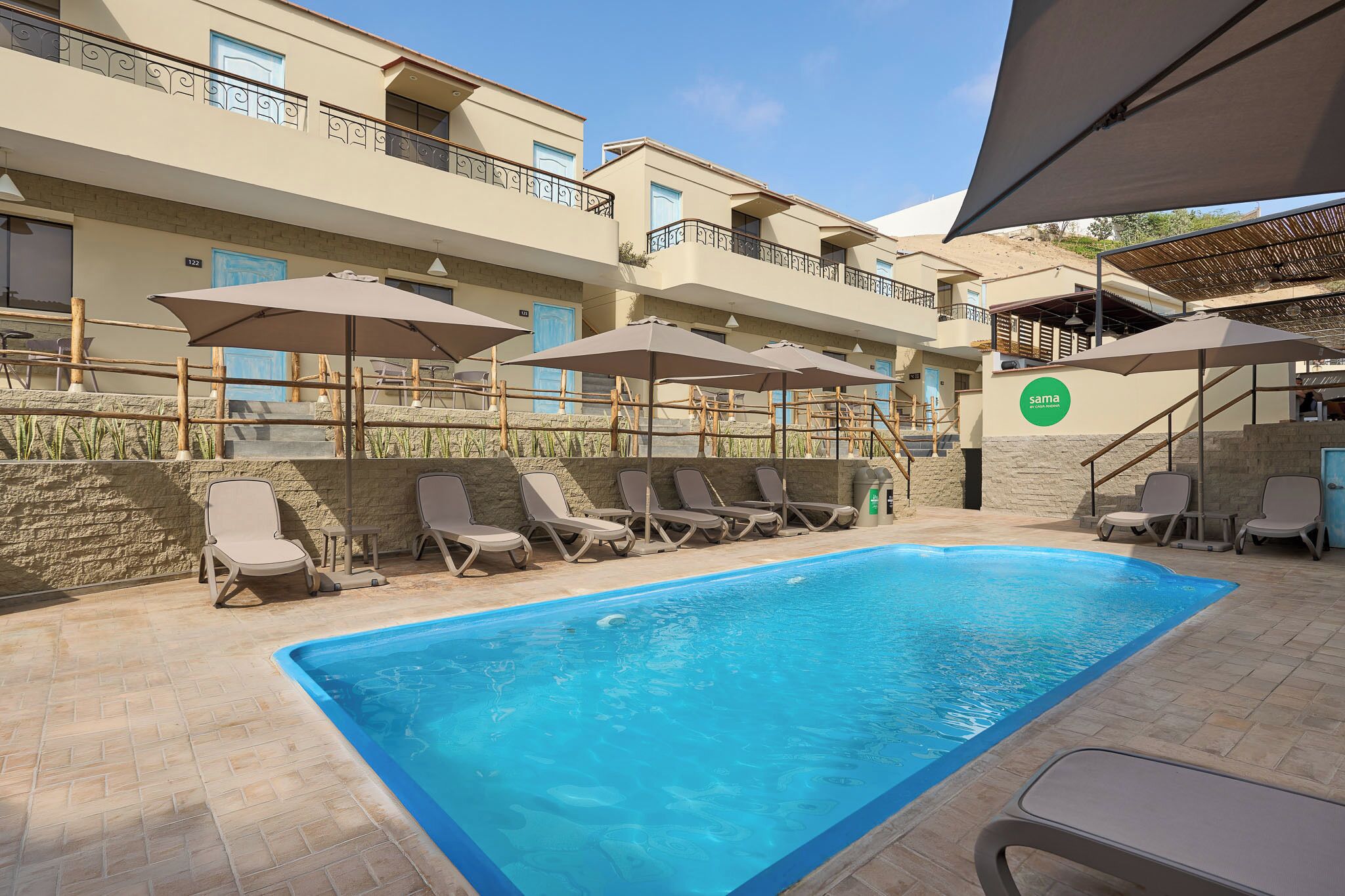 A swimming pool with lounge chairs and umbrellas, a stone wall, and a building with balconies.
