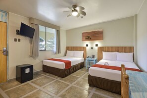 Habitación de hotel con dos camas, televisor, ventilador de techo, ventana con cortinas, una mesita y un refrigerador.