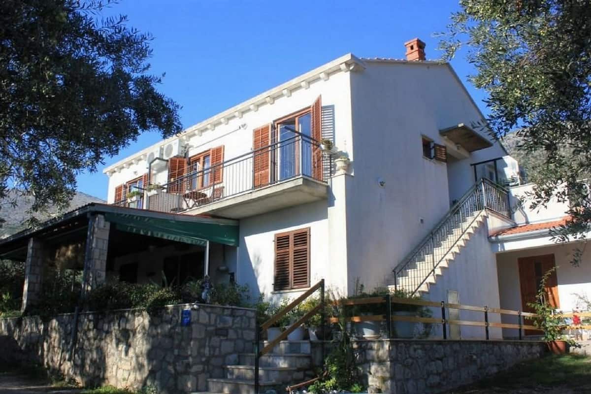 A two-story building with a balcony, stone steps, and a stone wall.