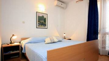 A bedroom with a wooden bed, two bedside tables with lamps, a wall-mounted air conditioner, and a window with curtains.