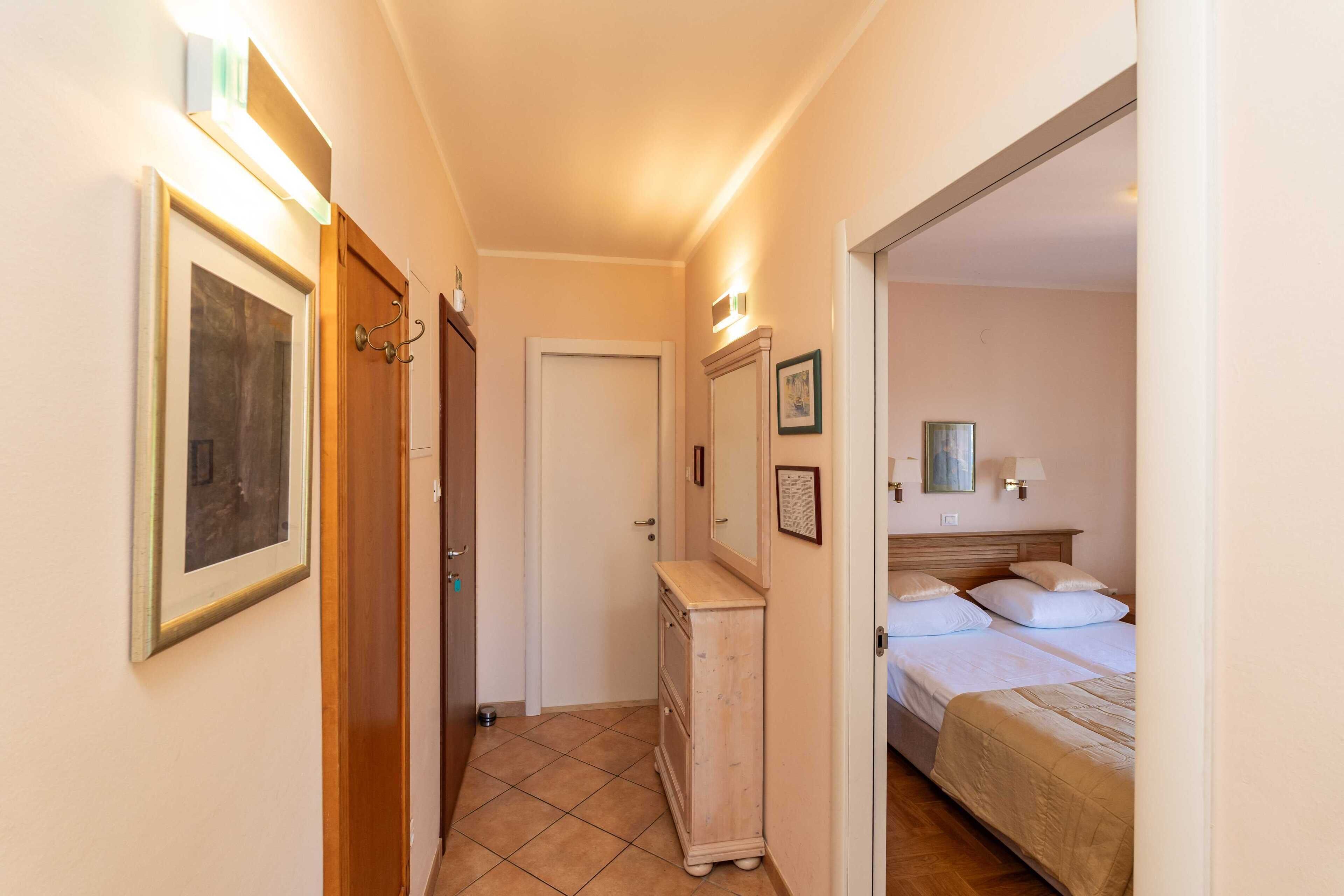 A narrow hallway leading to a bedroom with a bed, a dresser, and framed pictures on the walls.