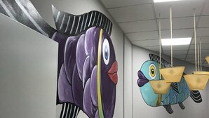 A room with a white table and chairs, a ceiling with fluorescent lights, and a mural of two colorful birds on the wall. - Albergue Augas Quentes - Hostel (Ourense)