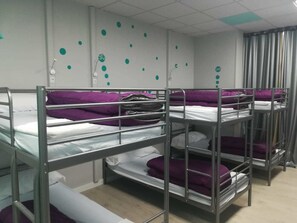 A dormitory room with bunk beds, each with a purple blanket. There are white walls and a ceiling with a grid pattern.
