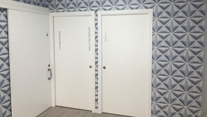 A room with three white doors labeled "Living Room," "Sala de Estar," and "Room 1." The walls have a geometric pattern. - Albergue Augas Quentes - Hostel (Ourense)
