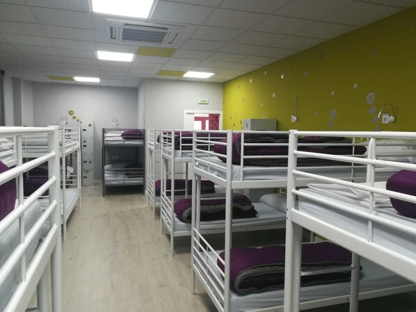 A dormitory room with bunk beds, a yellow wall, and a door in the background.