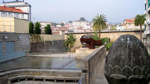 A stone fountain in a courtyard with a view of buildings in the background. - Albergue Augas Quentes - Hostel (Ourense)