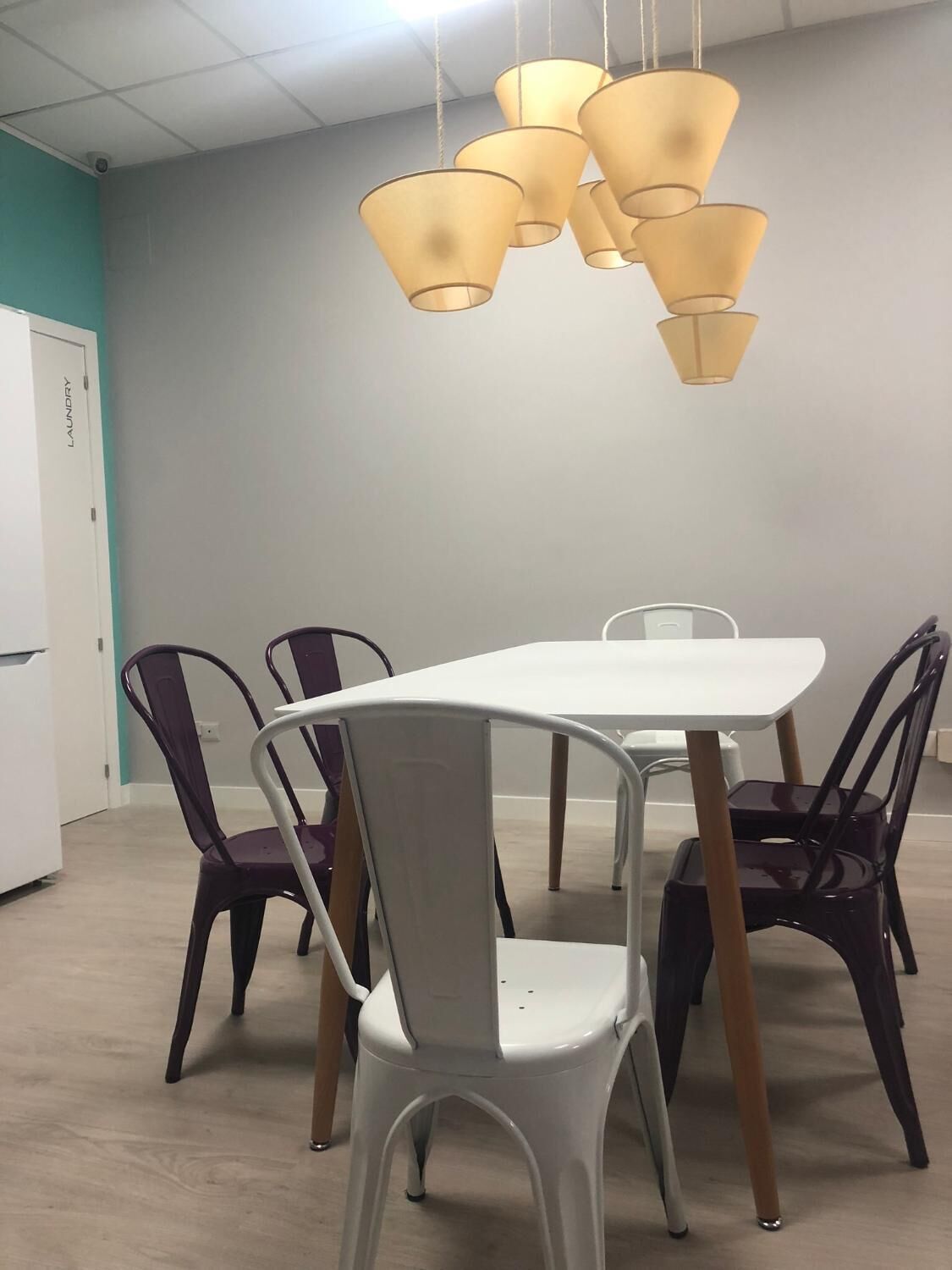 Un salón de conferencias con una mesa blanca, cuatro sillas y una lámpara colgante.