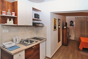 A compact kitchen with a microwave, kettle, and sink. There are wooden cabinets and a small table with a red tablecloth.
