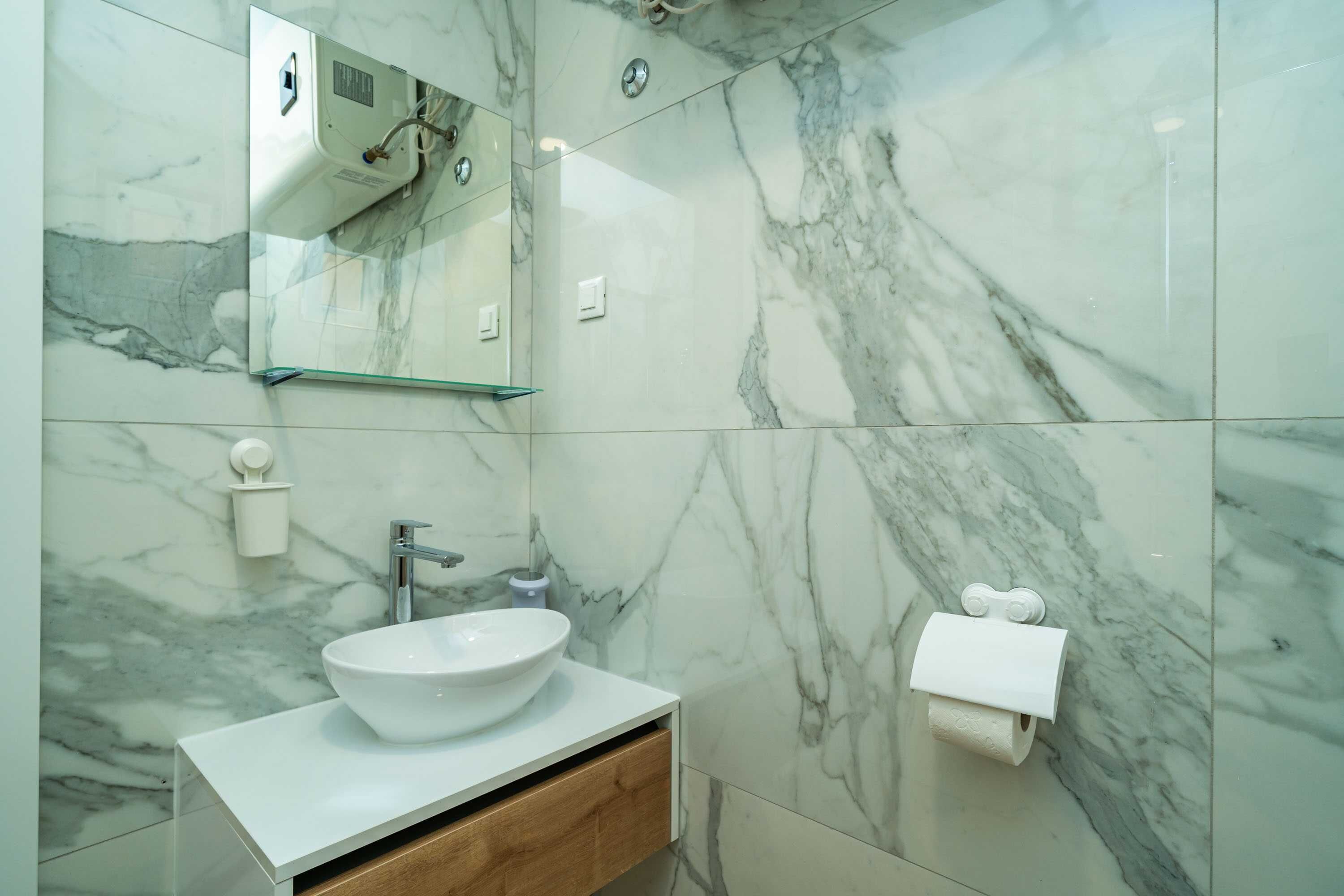 A bathroom with a marble wall, a white sink, a mirror, and a towel dispenser.
