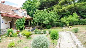Una casa con techo de tejas, un porche cubierto y un jardín con diversas plantas y un sendero.