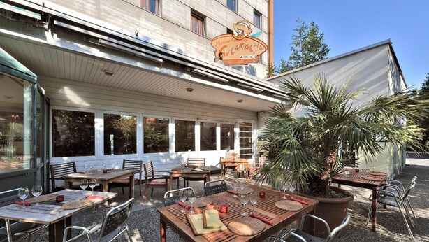 An outdoor seating area with tables and chairs, a large potted plant, and a building with a sign that reads 'Cucaracha & Bar'.