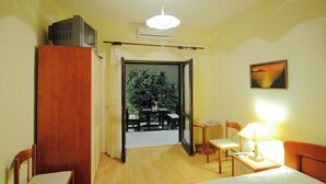Quarto de hotel com uma cama, uma mesa com luminária, uma cadeira, uma TV sobre um móvel e um quadro na parede.