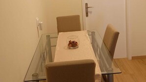 Uma área de refeições com mesa de vidro, duas cadeiras, uma porta e um interruptor de luz fixado na parede.