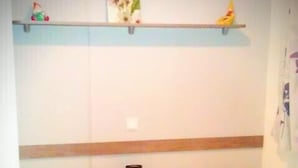 Een slaapkamer met twee bedden, elk voorzien van een geruit sprei, een nachtkastje met een lamp en een plank boven de bedden.