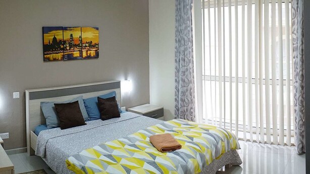 A bedroom with a bed, a nightstand, a wall-mounted lamp, and a window with blinds. - Flat in Gzira 2 minutes from the sea (Gzira)