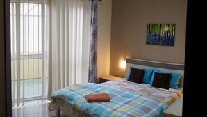 A bedroom with a bed, a nightstand, a painting, and a window with blinds. - Flat in Gzira 2 minutes from the sea (Gzira)