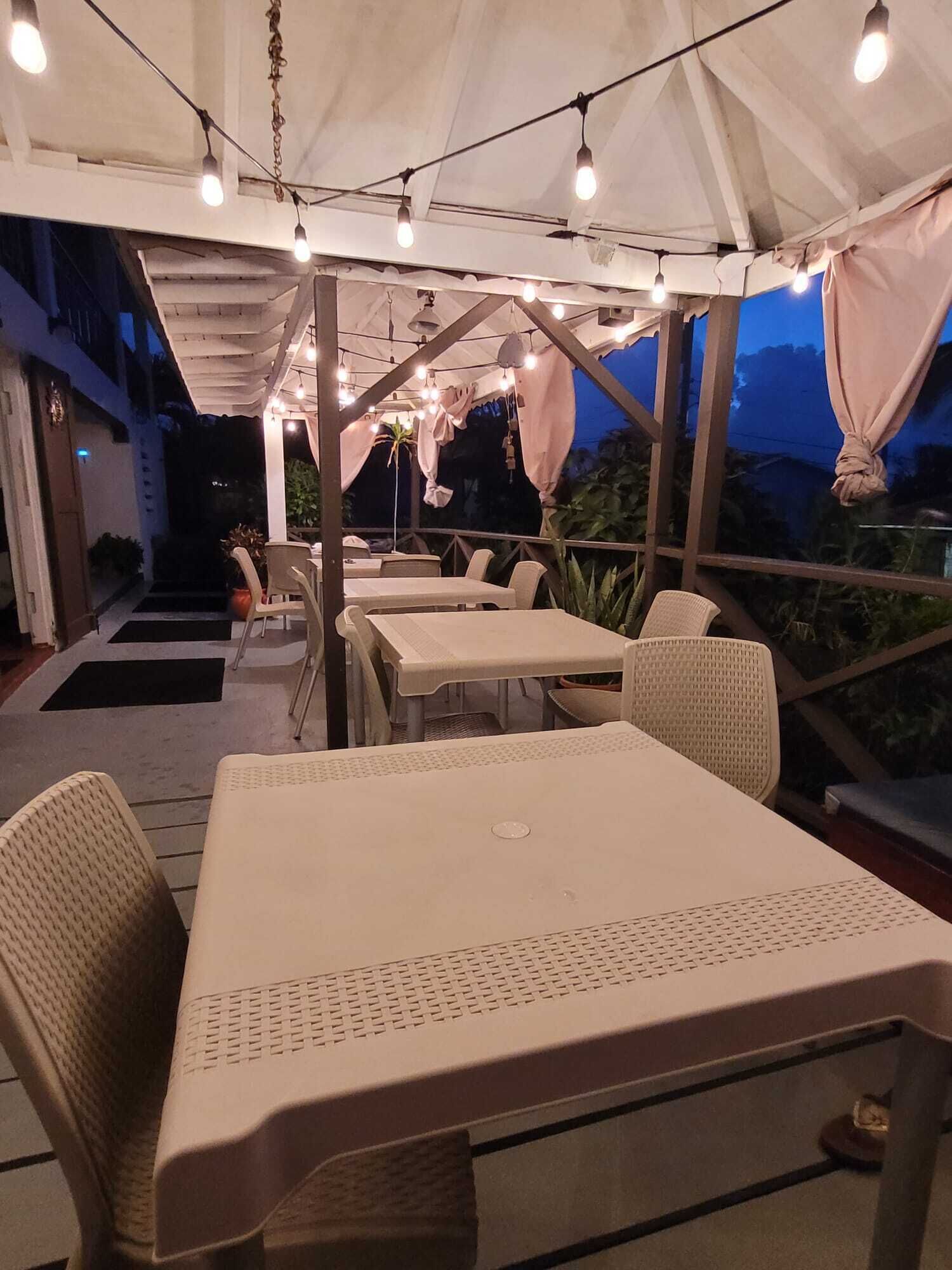 An outdoor patio area with tables and chairs, string lights, and a covered structure.