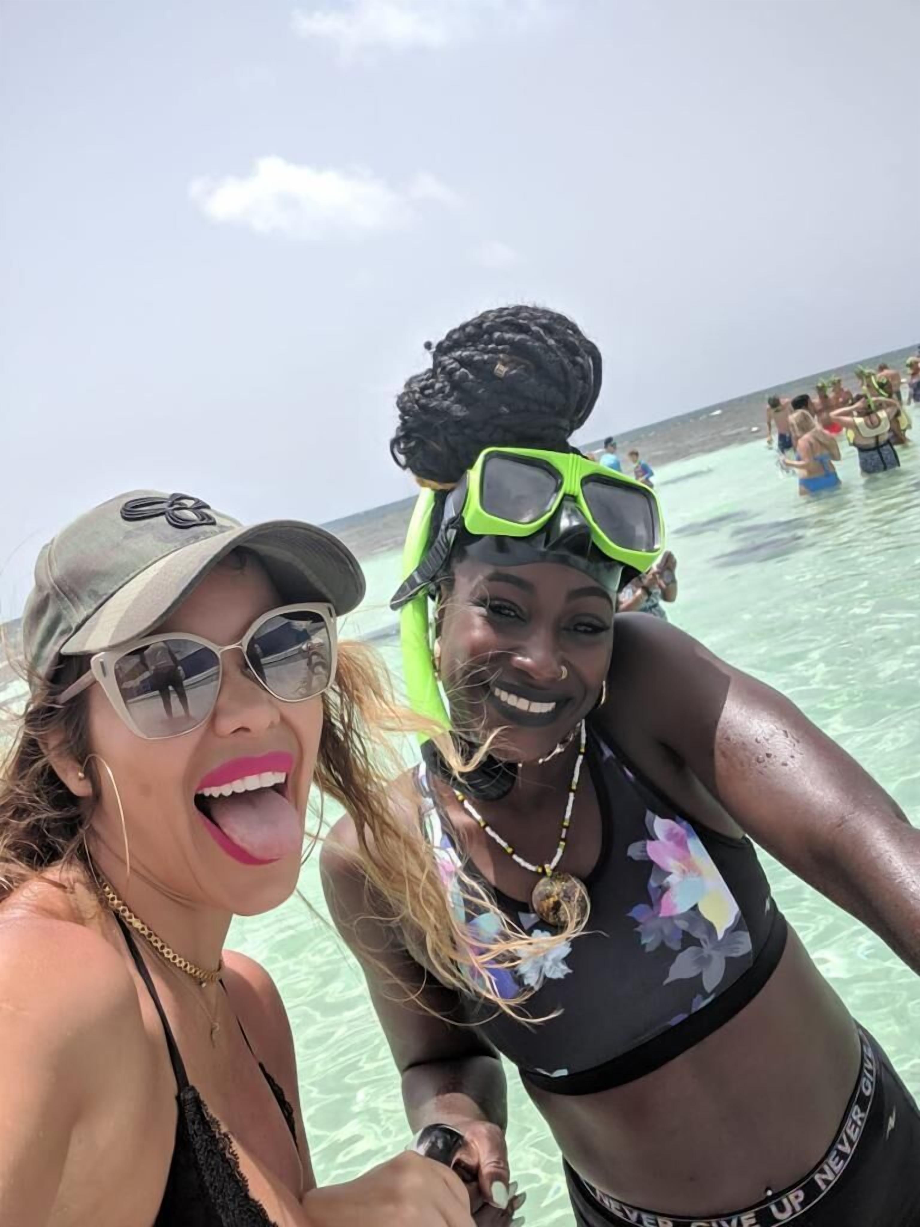 Two people snorkeling in clear water with a beach and other people in the background.