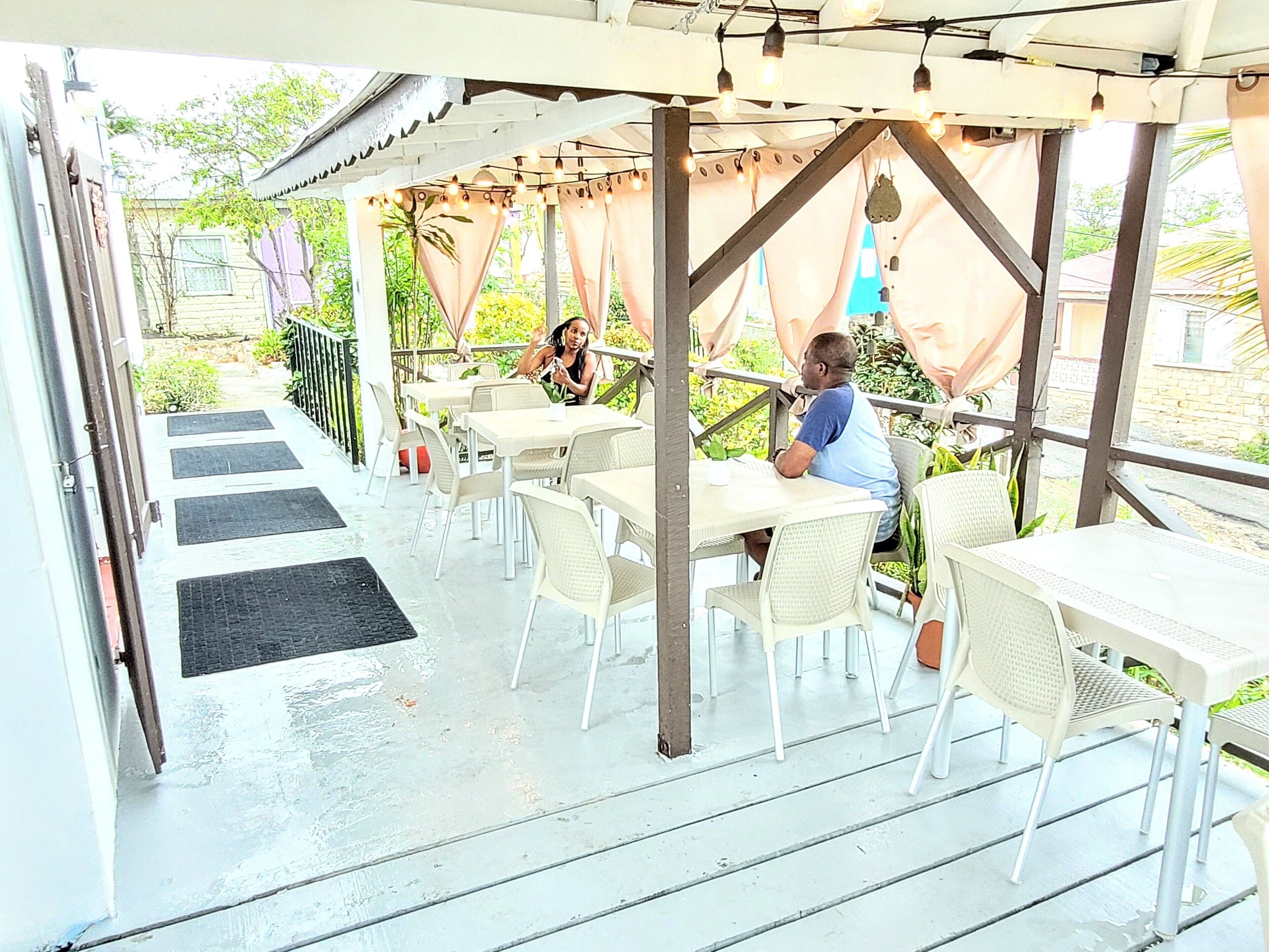 An outdoor patio with tables and chairs, a covered seating area, and a view of the surrounding greenery.