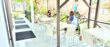 An outdoor patio with tables and chairs, a covered seating area, and a view of the surrounding greenery.