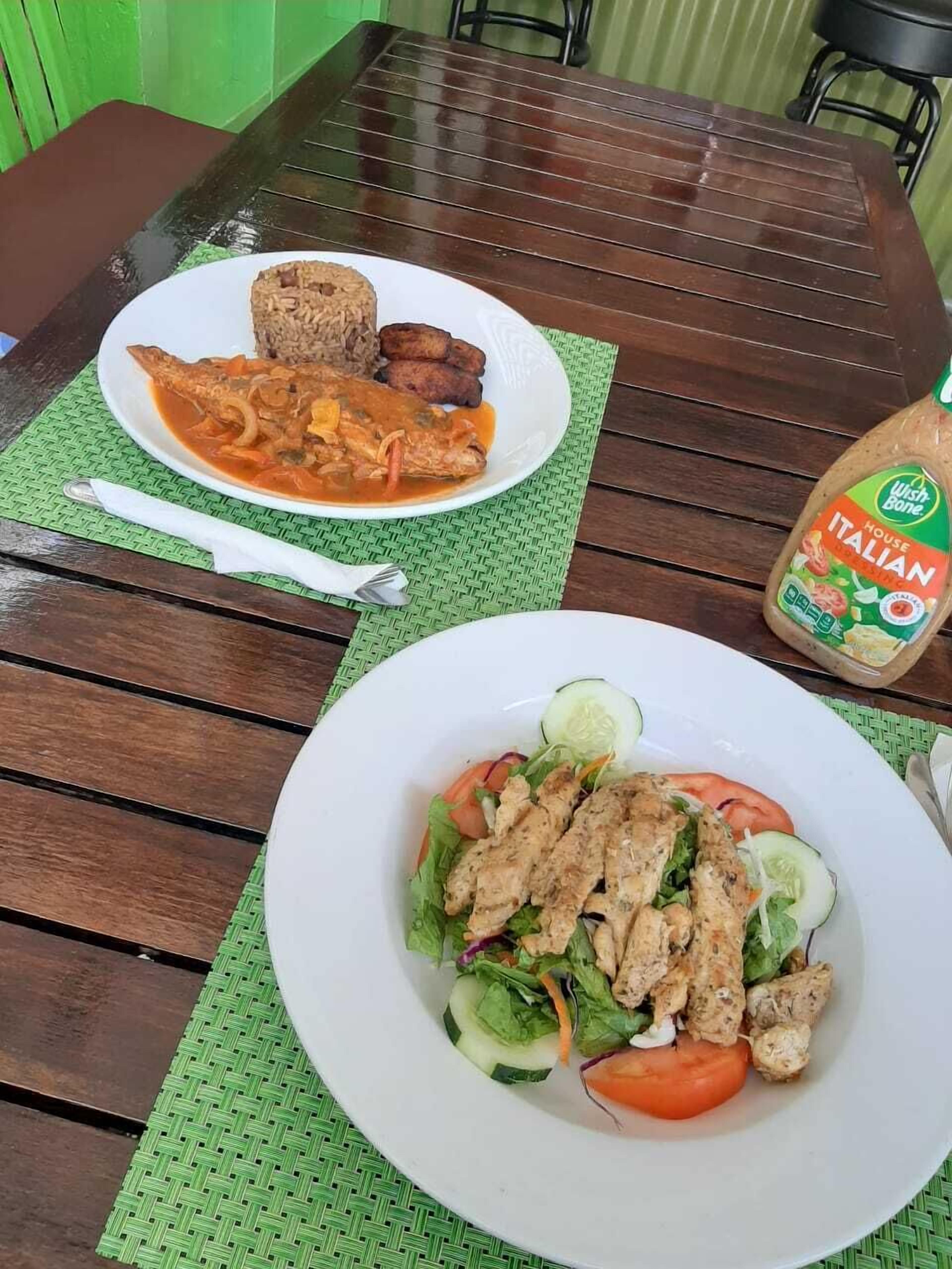 A wooden table with two plates of food, one with a salad and the other with a meal including rice and fried items.