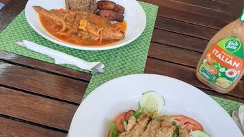 A wooden table with two plates of food, one with a salad and the other with a meal including rice and fried items.