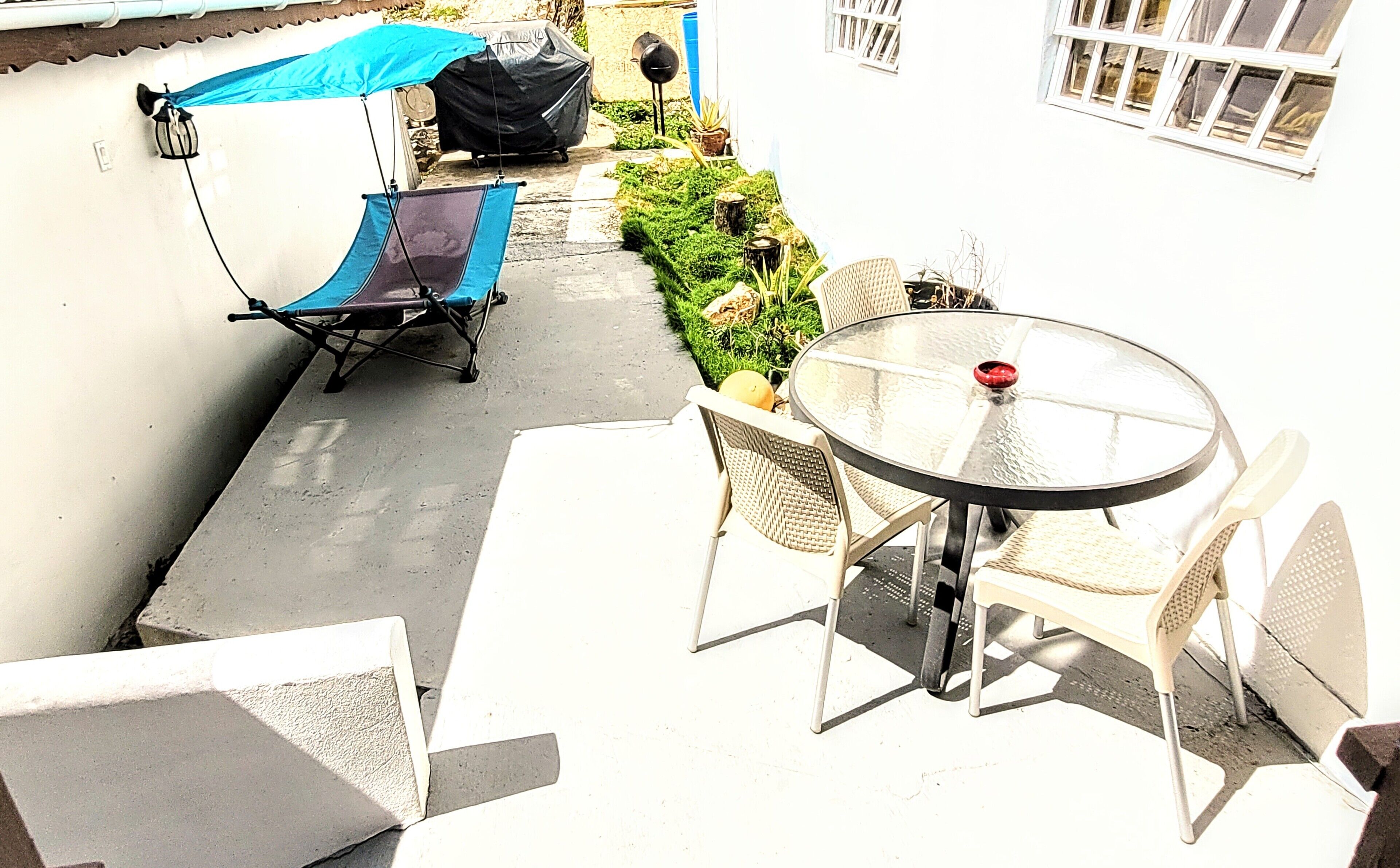 A patio area with a table and chairs, a covered chair, and a grill.