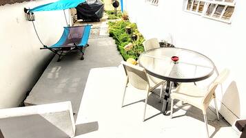 A patio area with a table and chairs, a covered chair, and a grill.