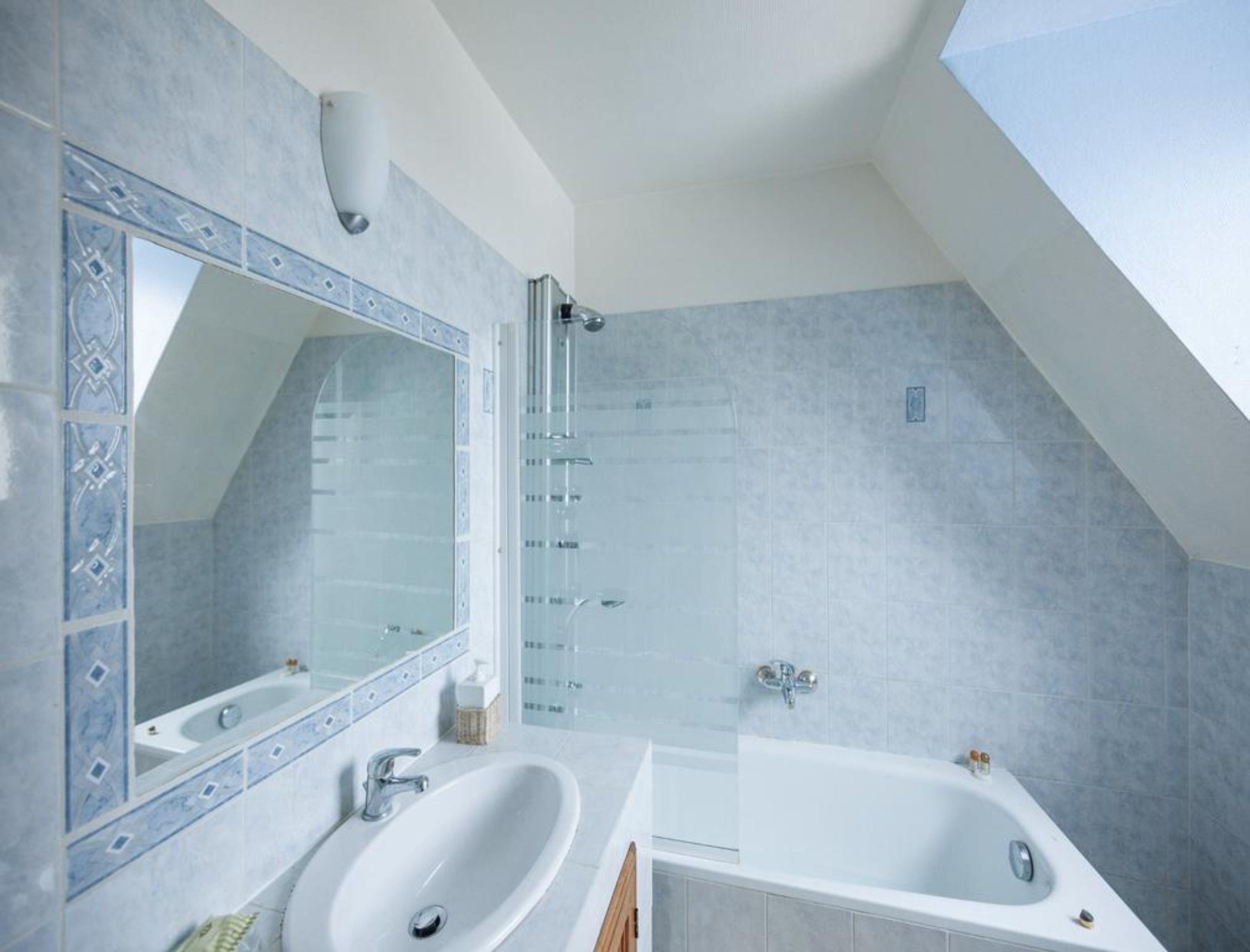 Une salle de bain moderne dotée d’un puits de lumière, d’un grand miroir, de deux vasques et d’une baignoire.